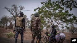 FILE - A police officer and a soldier from Benin stop a motorcyclist at a checkpoint outside Porga, Benin, March 26, 2022. 