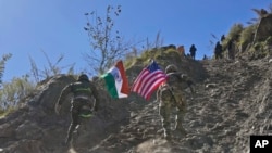 An Indian and U.S. army soldier, each carrying their respective countries' flags, run up a hill during joint Indo-U.S. military exercises in the Indian state of Uttarakhand, Nov. 30, 2022.