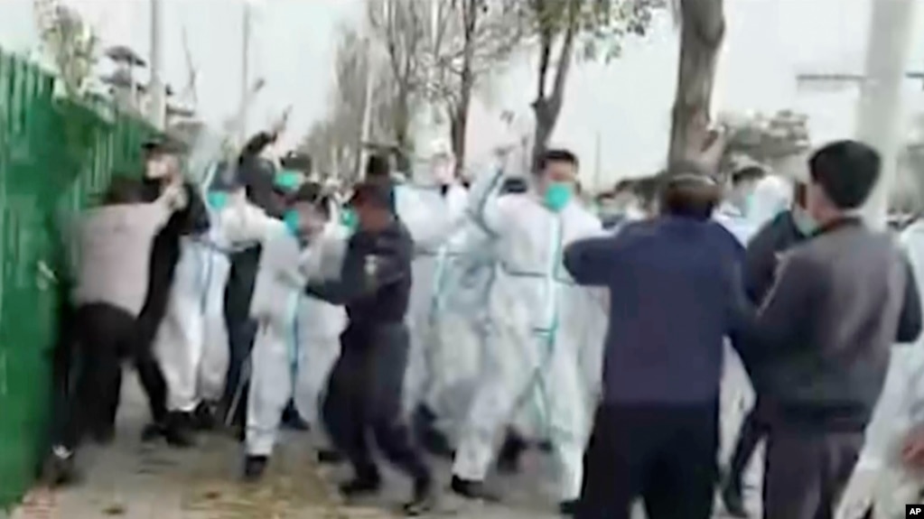 中国河南郑州富士康代工厂里身穿防护服的警察和保安殴打参加示威活动的工人。(美联社2022年11月23日)(photo:VOA)