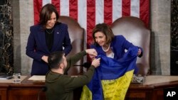 Vice President Kamala Harris, left, and House Speaker Nancy Pelosi, right, smile as Ukrainian President Volodymyr Zelenskyy presents lawmakers with a Ukrainian flag — signed by troops serving in Ukraine's contested Donetsk province — as he addresses a joint meeting of Congress in Washington, Dec. 21, 2022.