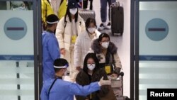 身穿防护服的韩国军人指引从中国抵达仁川国际机场的乘客进行新冠核酸检测。（2023年1月4日）