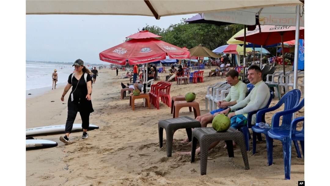 Turis tengah menikmati suasana pantai di Bali, Sabtu, 12 November 2022. Perekonomian Bali sedang membaik tetapi hanya menarik sepertiga dari wisatawan yang biasanya datang sebelum pandemi. (AP/Firdia Lisnawati)