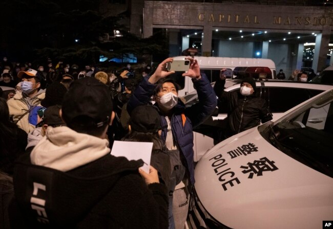 Protesters pass near a police car in Beijing, Sunday, Nov. 27, 2022. (AP Photo/Ng Han Guan)