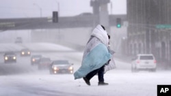 Seseorang warga menyelimuti tubuhnya dengan selimut, saat melintasi jalan yang tertutup salju di St. Louis, Kamis, 22 Desember 2022. (AP/Jeff Roberson)