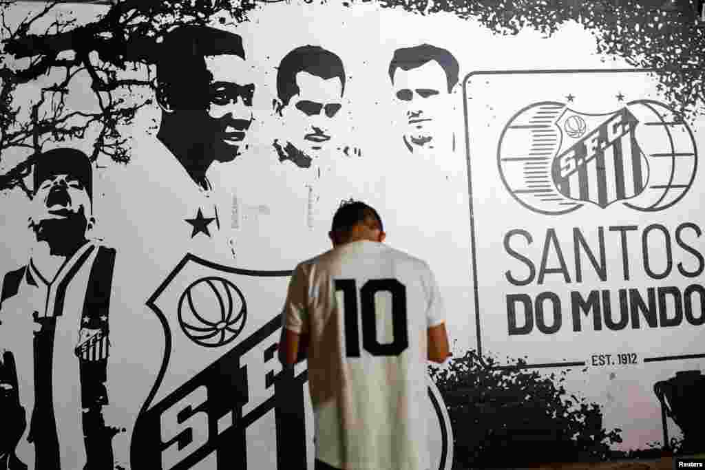 A person stands in front of an image depicting Brazilian soccer legend Pele as people gather to mourn his death, in Santos, Brazil, Dec. 29, 2022.