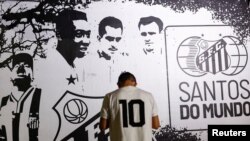 Seseorang berdiri di depan gambar legenda sepak bola Brazil Pele saat orang-orang berkumpul untuk berduka atas kematiannya, di Santos, Brazil, 29 Desember 2022. (Foto: Reuters)