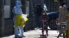 A child wearing a face mask and riding on a scooter passes by a worker in protective suit on his way to collect COVID samples from the lockdown residents in Beijing, Dec. 1, 2022. 