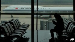 FILE - A passenger checks her phone as an Air China passenger jet taxis past at Beijing Capital International airport, in Beijing, Oct. 29, 2022. China will drop a COVID-19 quarantine requirement for passengers arriving from abroad starting Jan. 8, 2023.