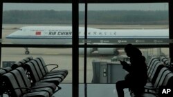 FILE - A passenger checks her phone as an Air China passenger jet taxis past at Beijing Capital International Airport, in Beijing, Oct. 29, 2022. 