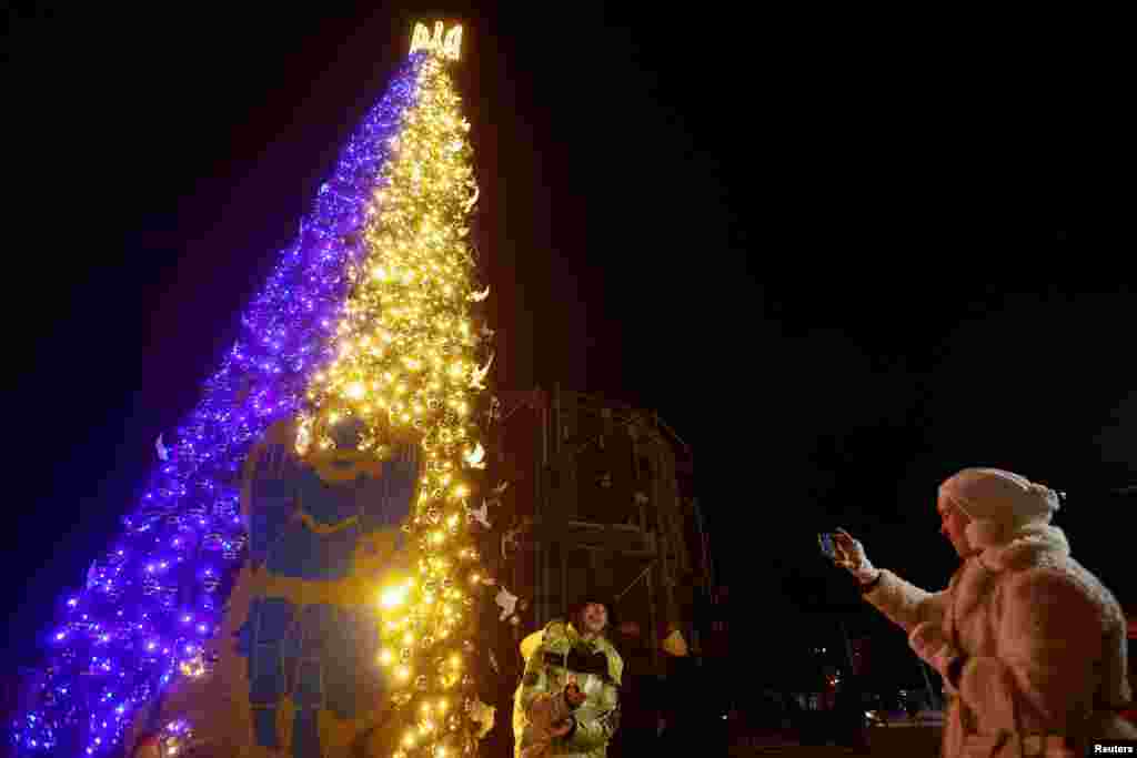 El árbol de Navidad no podía faltar en las celebraciones de fin de año. Con los colores de la bandera de Ucrania, en la Plaza Sofiyska, de Kiev, se alza el árbol frente al que una mujer canta villancicos.&nbsp;