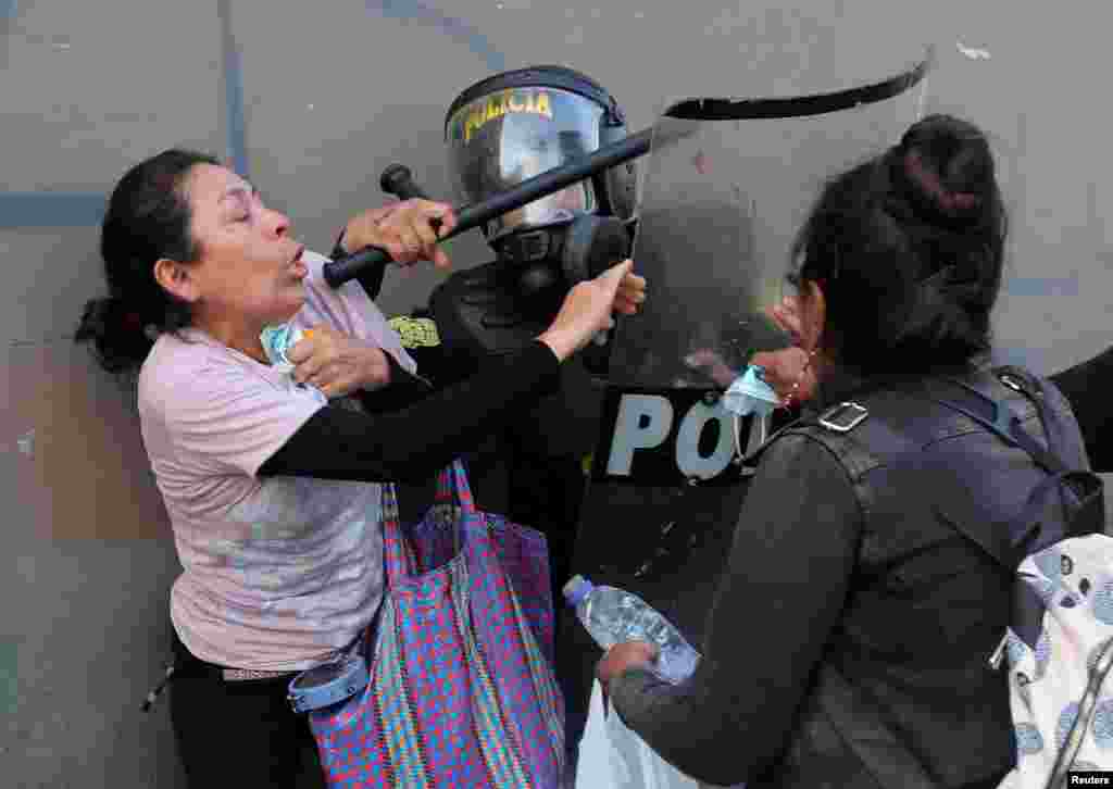 A woman struggles with a riot police officer during a protest after the ousting of Peruvian President Pedro Castillo, in Lima, Dec. 12, 2022.