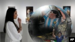 La artista paraguaya Lili Cantero, detrás de uno de sus balones pintados, con la imagen del fallecido as argentino Maradona, en una exposición en Katara Cultural Ville, en Doha, Qatar, el 24 de noviembre de 2022. (AP Foto/Jorge Sáenz)