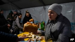 A volunteer gives free meal to people who lost electrical power after recent Russian rocket attack in a heating point in the town of Vyshhorod, north of Kyiv, Ukraine, Nov. 25, 2022.