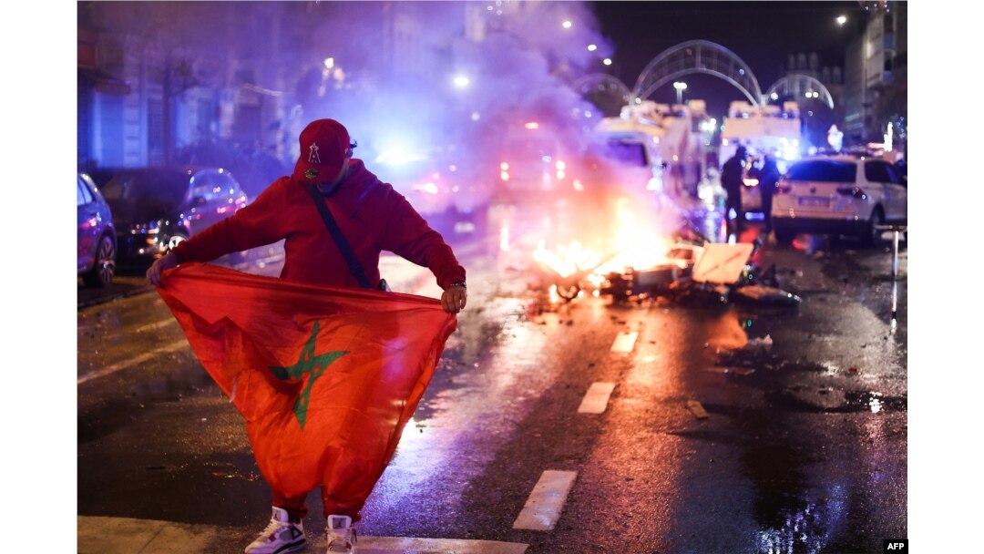 Seorang penggemar memegang bendera Maroko ketika skuter listrik terbakar di bagian belakang di sela-sela siaran langsung pertandingan sepak bola Grup F Piala Dunia 2022 Qatar antara Belgia dan Maroko, di Brussel, pada 27 November 2022. (Foto: AFP)