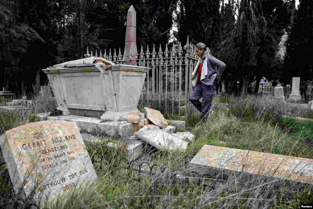 Iska, who works at the nearby church, inspects a vandalized tombstone at the Protestant Mount Zion Cemetery in Jerusalem.