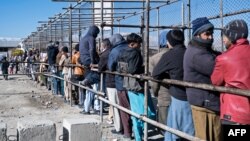FILE - Afghan men stand in a queue as they wait to receive food aid from a non-governmental organization (NGO) in Kabul, Jan. 3, 2023. Aid groups say they have been pushed against a wall by the Taliban prohibiting Afghan women from working for NGOs.
