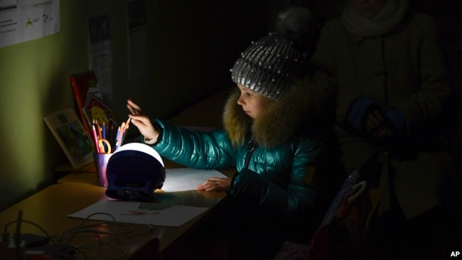 Alexandra, de 11 años, dibuja en un edificio escolar, un "Punto de invencibilidad", una estación de ayuda construida por el gobierno que permite cargar teléfonos con la ayuda de generadores, sirve comida, bebidas y la posibilidad de calentarse, en Kramatorsk, Ucrania, dic. 5, 2022.