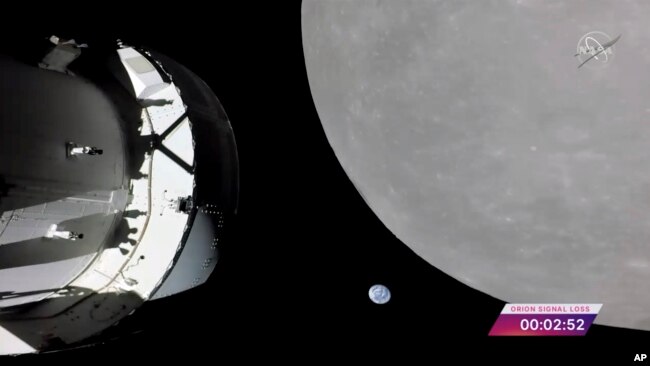 This screengrab from NASA TV shows NASA's Orion capsule, left, nearing the moon, right, Monday, Nov. 21, 2022. At center is Earth. (NASA via AP)