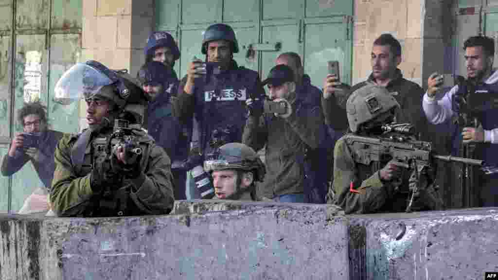 Israeli soldiers, surrounded by journalists, take cover behind concrete barriers during clashes with Palestinian youths protesting the death of Palestinian prisoner Nasser Abu Hamed in Israeli prison, in city center of Hebron in the occupied West Bank.