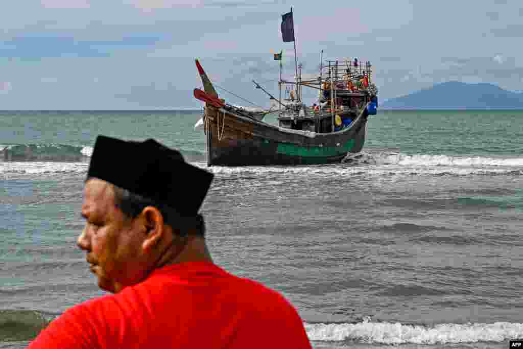 Човек стои во близина на брод што го користеле бегалците Рохинџа за да пристигнат на плажата Ламга, провинцијата Ачех, Индонезија.