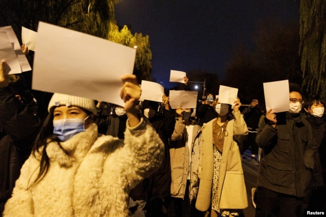 People hold white sheets of paper in protest of coronavirus disease (COVID-19) restrictions, after a vigil for the victims of a fire in Urumqi, as outbreaks of the coronavirus disease continue in Beijing, China, November 27, 2022. (REUTERS/Thomas Peter)