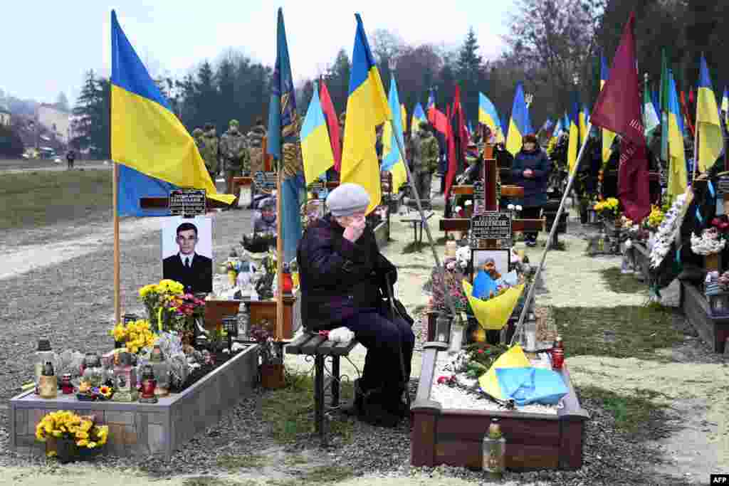 An elderly woman grieves next to the grave of a Ukrainian soldier during Ukraine&#39;s Army Day at Lychakiv Cemetery in the western city of Lviv.