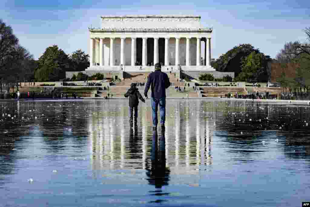 Seorang pria dan anak laki-laki berjalan melintasi Reflecting Pool yang membeku menuju Lincoln Memorial di National Mall di Washington, DC, pada 26 Desember 2022. (Foto: AFP/Jim WATSON)