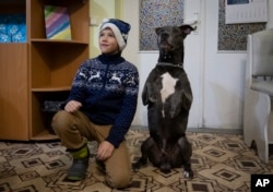 A boy poses for photo with an American Pit Bull Terrier "Bice" in the Center for Social and Psychological Rehabilitation in Boyarka close Kyiv, Ukraine, Wednesday, Dec. 7, 2022. (AP Photo/Vasilisa Stepanenko)