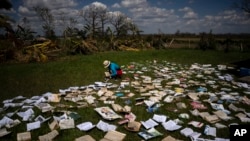 Seorang guru tampak mengeringkan buku-buku yang terendam selama badai Ian melanda La Coloma, Provinsi Pinar del Rio, Kuba, pada 5 Oktober 2022. (Foto: AP/Ramon Espinosa)