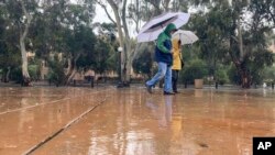 Pedestrians carry umbrellas as they walk in the rain in Stanford, California, Dec. 31, 2022. Officials warned that rivers and streams could overflow and urged residents to get sandbags ready.