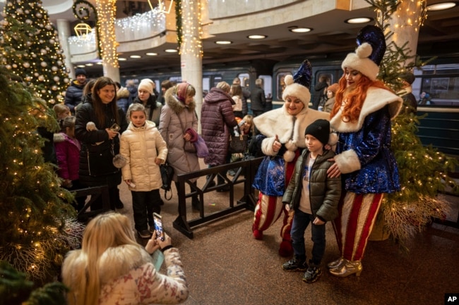 Women dressed in costumes pose with a boy for a photograph at the subway station "University" decorated for Christmas and New Year in Kharkiv, Ukraine, Saturday, Dec. 31, 2022. (AP Photo/Evgeniy Maloletka)