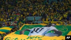 Aficionados brasileños sostienen una bandera brasileña gigante con una imagen del exjugador brasileño Pelé con un mensaje que dice en inglés "Pele, mejórate pronto".