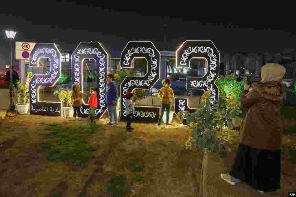 Una mujer toma fotografías de sus hijos cerca de un letrero iluminado de 2023 en la ciudad de Nasiriyah, en el sur de Irak, en medio de las celebraciones de Año Nuevo, a última hora del 31 de diciembre de 2022. [AFP]