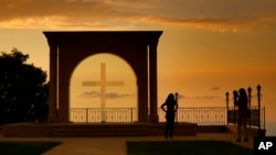 FILE - A woman uses her mobile phone to take a picture of her friend as the sun sets behind Saint Simon Church in Ghosta, in east Beirut, Lebanon, Oct. 8, 2022. 