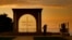 FILE - A woman uses her mobile phone to take a picture of her friend as the sun sets behind Saint Simon Church in Ghosta, in east Beirut, Lebanon, Oct. 8, 2022. 