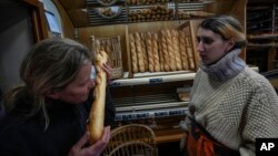 Bakery owner Florence Poirier, left, smells a fresh baguette as Mylene Poirier stands next to her at a bakery, in Versailles, France, Nov. 29, 2022. The humble baguette is being added to the U.N.'s list of intangible cultural heritage.