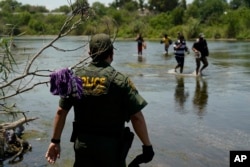 FILE - In this June 15, 2021, file photo, a Border Patrol agent watches as a group of migrants walk across the Rio Grande on their way to turning themselves in upon crossing the U.S.-Mexico border in Del Rio, Texas. (AP Photo/Eric Gay, File)