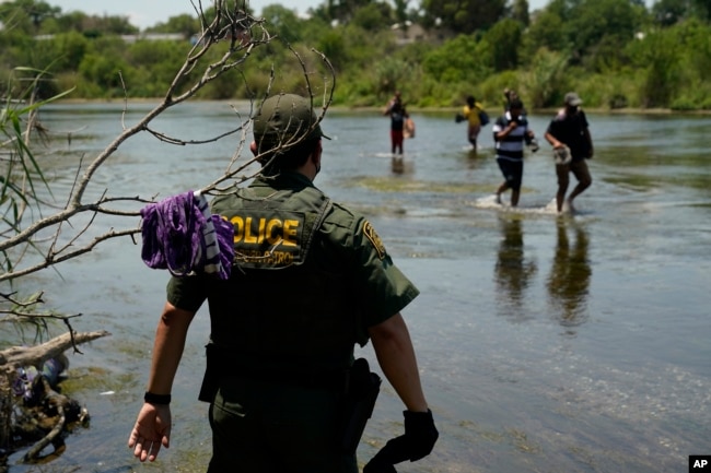 FILE - In this June 15, 2021, file photo, a Border Patrol agent watches as a group of migrants walk across the Rio Grande on their way to turning themselves in upon crossing the U.S.-Mexico border in Del Rio, Texas. (AP Photo/Eric Gay, File)