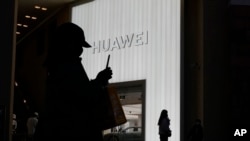 FILE - Shoppers are silhouetted outside a Huawei retail store in Beijing, China, Dec. 30, 2022. 