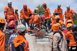 Tim penyelamat menggunakan gergaji saat mereka mencoba mengevakuasi jenazah korban gempa bumi dari bawah reruntuhan bangunan yang runtuh di Cianjur, Jawa Barat, Selasa, 22 November 2022. (AP Photo/Tatan Syuflana)