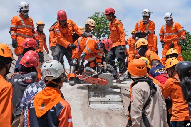 Tim penyelamat menggunakan gergaji saat mereka mencoba mengevakuasi jenazah korban gempa bumi dari bawah reruntuhan bangunan yang runtuh di Cianjur, Jawa Barat, Selasa, 22 November 2022. (AP Photo/Tatan Syuflana)