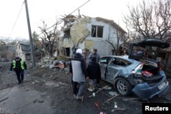 People stand next to a house and car damaged during a Russian missile strike in Kyiv, Ukraine, Dec. 31, 2022.