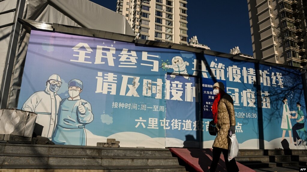 一名女子走过北京街头一幅抗疫宣传画。（2022年12月11日）(photo:VOA)