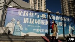 一名女子走過北京街頭一幅抗疫宣傳畫。（2022年12月11日）