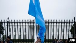 FILE - A man holds the Uyghur flag on Pennsylvania Avenue in front of the White House during a protest last year against the Chinese Communist Party. 