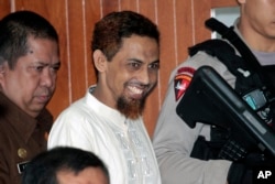 Pelaku terorisme Umar Patek, tengah, tersenyum saat memasuki ruang sidang untuk menghadiri persidangannya di pengadilan negeri di Jakarta, 20 Februari 2012. (Foto: AP)