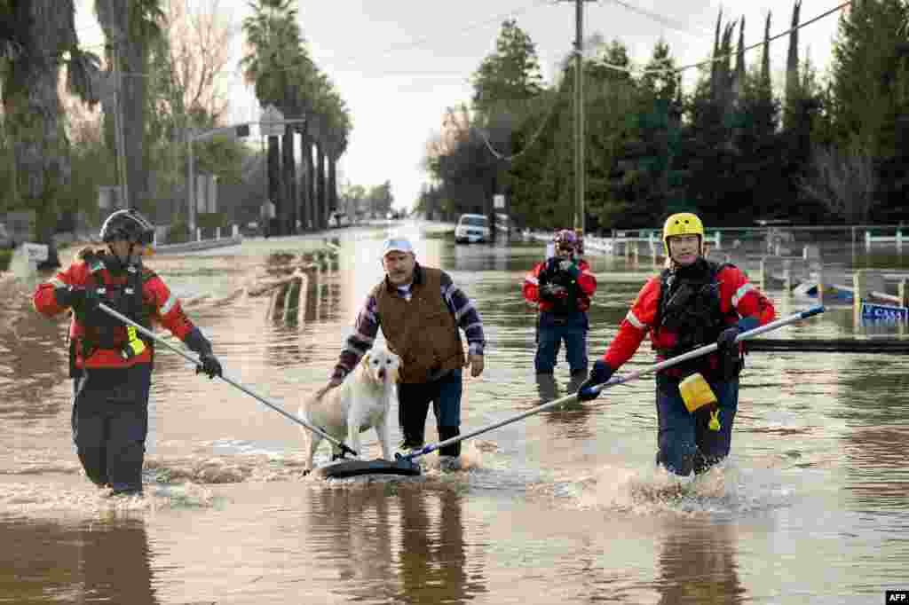 San Diego firefighters help Humberto Maciel rescue his dog from their flooded home in Merced, California, Jan. 10, 2023.&nbsp;Relentless storms were ravaging California again, the latest period of extreme weather that has left 14 people dead. Strong storms caused flash flooding, closed major highways, toppled trees and swept away cars and people.