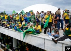 Para pengunjuk rasa, pendukung mantan presiden Brazil Jair Bolsonaro, berdiri di atap gedung Kongres Nasional setelah mereka menyerbunya, di Brasilia, Brazil, Minggu, 8 Januari 2023. (Foto: AP/Eraldo Peres)