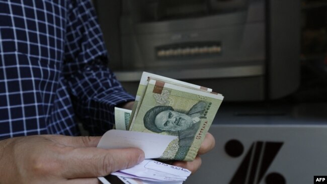 FILE - A man withdraws Iranian Rial notes from an automated teller machine in the capital Tehran on July 31, 2018. 