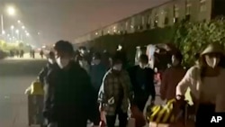 FILE - In this photo taken from video footage and released by Hangpai Xingyang, people with suitcases and bags are seen leaving from a Foxconn compound in Zhengzhou in central China's Henan Province on Oct. 29, 2022. 